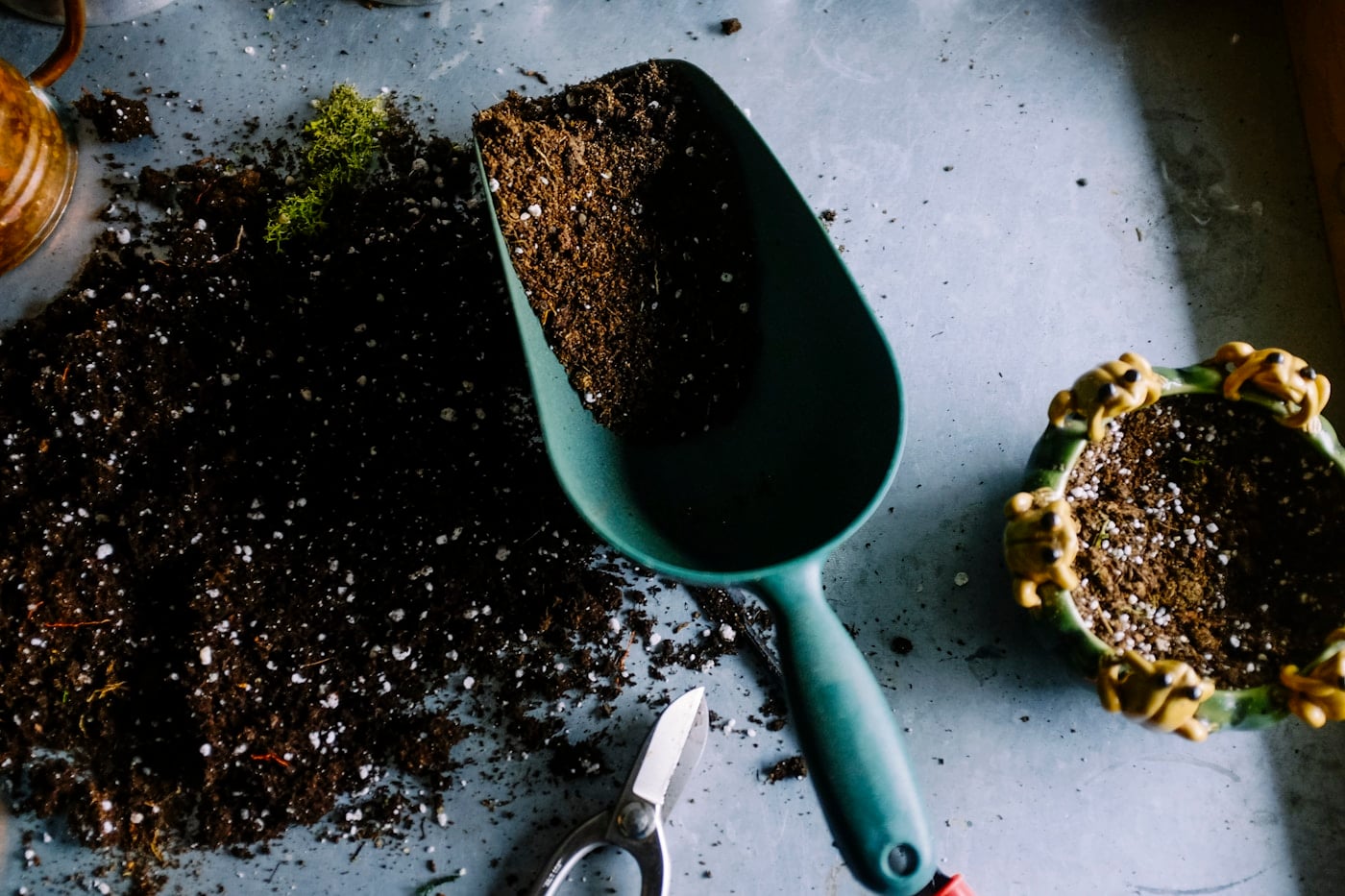 A garden trowel and plant pots surrounded by rich soil on a planting bench